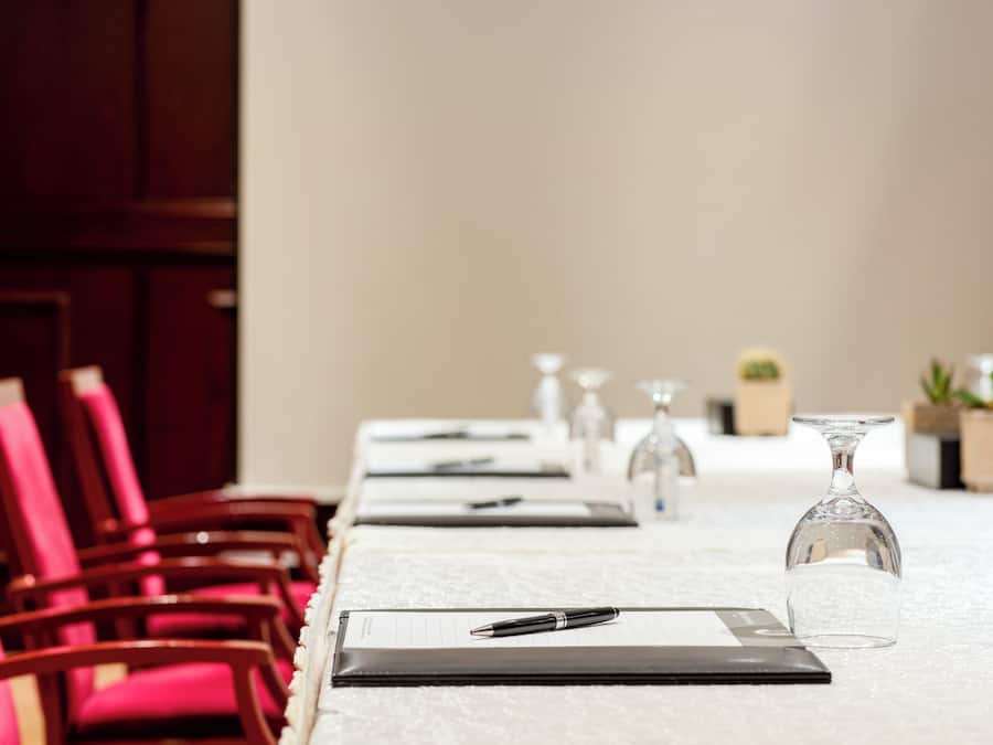 Une salle de conférence dotée d’une longue table, bordée de chaises, et équipée de stylos, de blocs-notes et de verres.