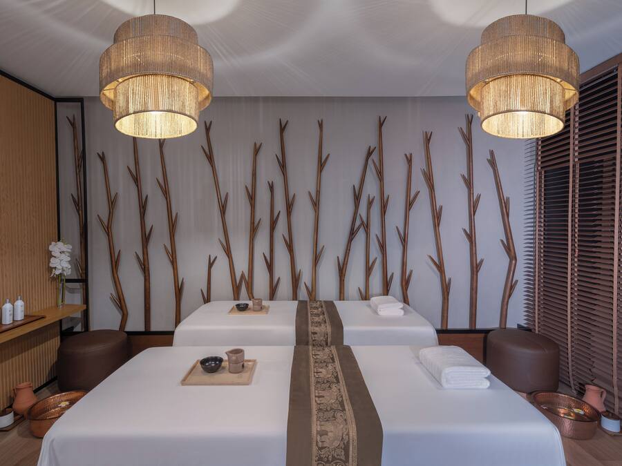A spa room with two beds, wooden decor, and a large window with blinds.