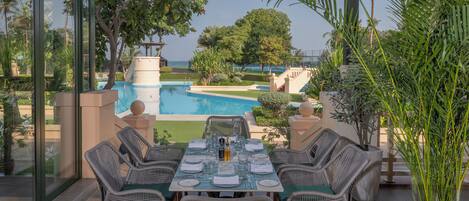 Un área de comedor al aire libre con vistas a una piscina y palmeras.