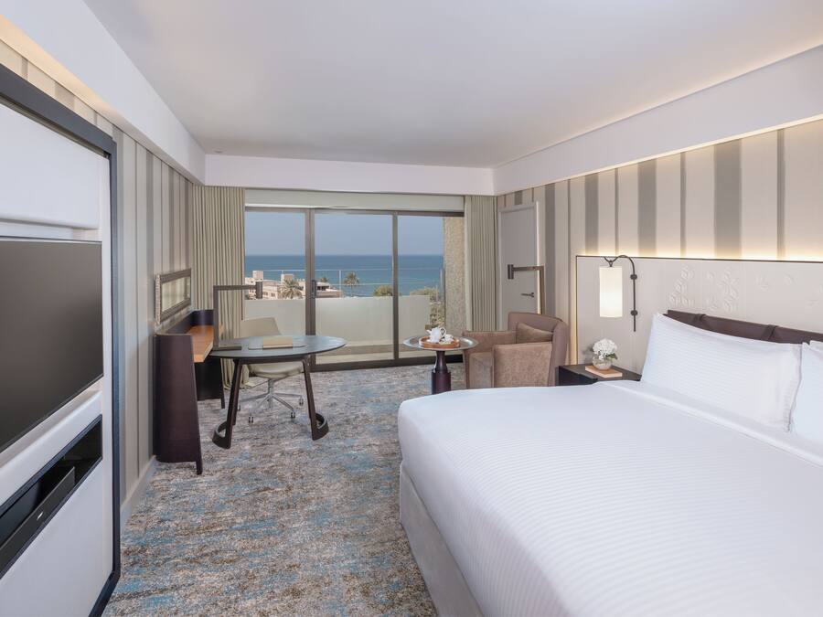 Una habitación de hotel con una cama, un escritorio, una silla, un televisor y vistas al océano.