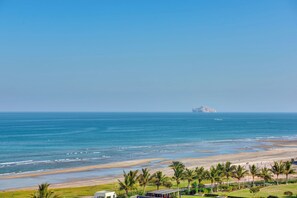 Un paisaje costero con playa, palmeras y una isla distante.