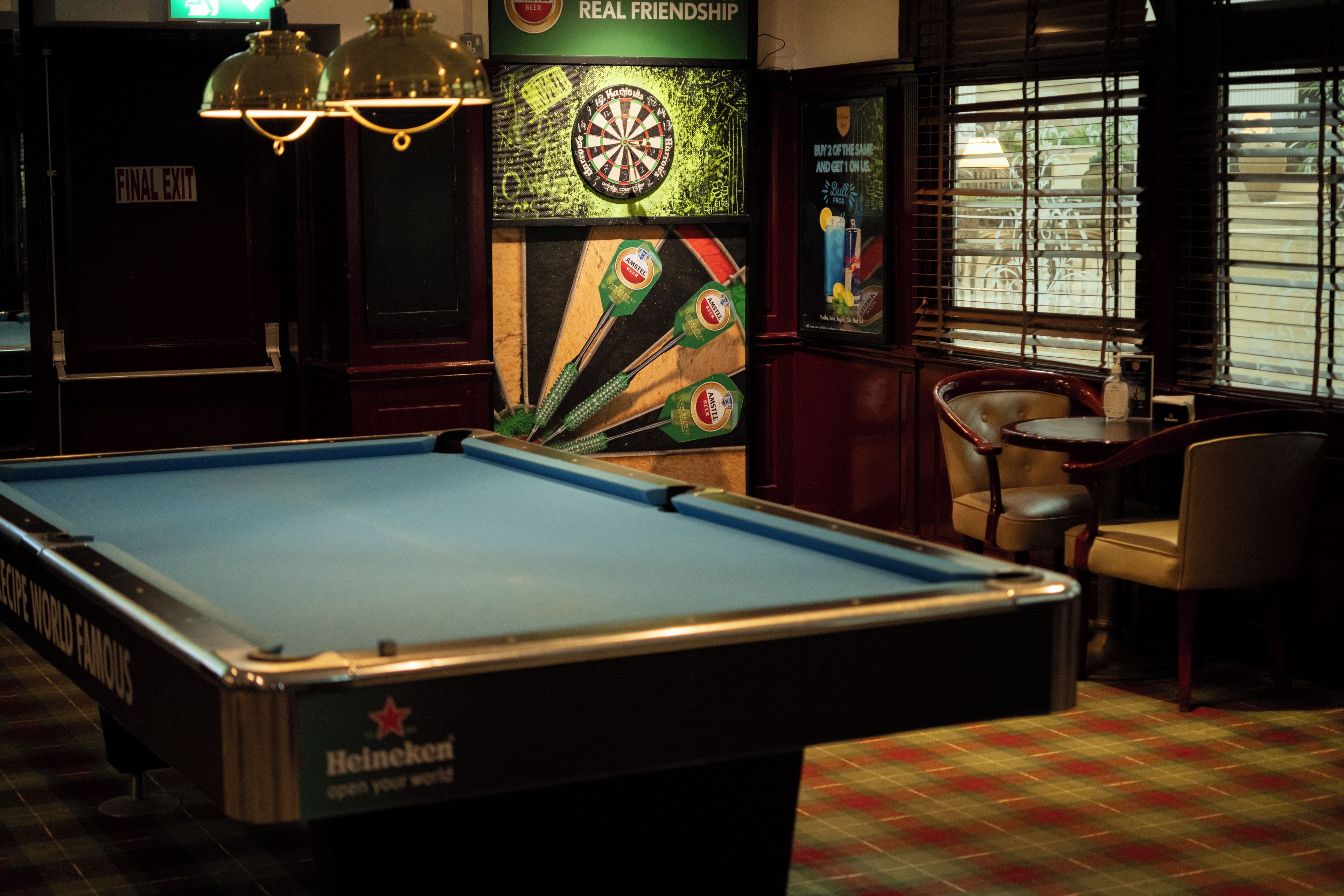 A billiards table with a Heineken logo, a dartboard, and a dartboard with a dart in the center.