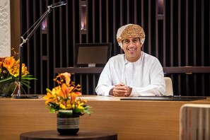 A man seated at a desk with a computer monitor, a microphone stand, and a vase of flowers. - InterContinental Muscat by IHG (Muscat)