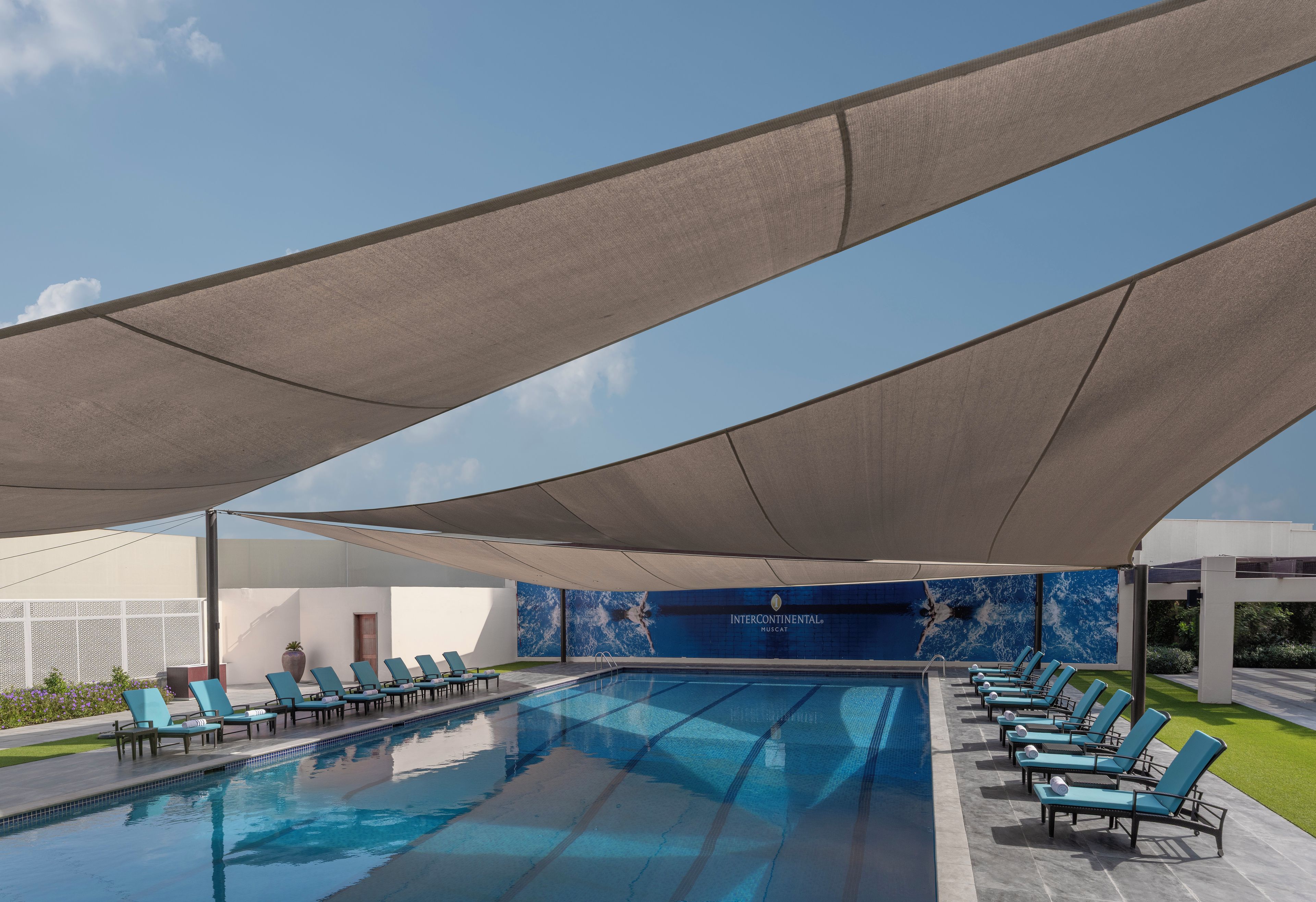 Una piscina con sillas de descanso y una zona sombreada, con un mural en la pared y el texto "Intercontinental" a la vista.