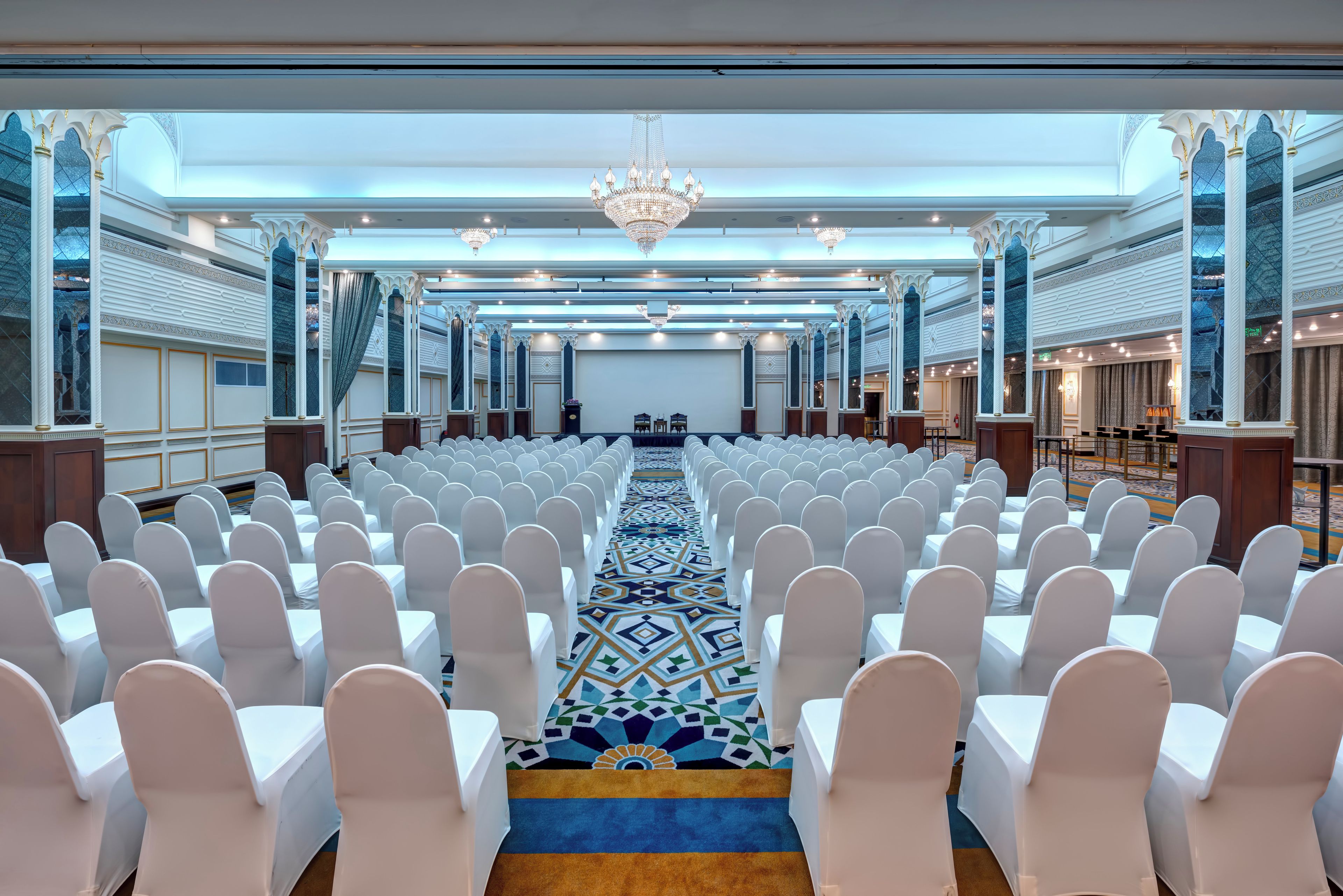 A conference room with rows of white chairs, a patterned carpet, and a chandelier.
