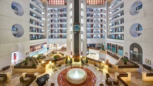 A multi-level hotel lobby with a central atrium, multiple floors with balconies, and a fountain in the middle. - InterContinental Muscat by IHG (Muscat)