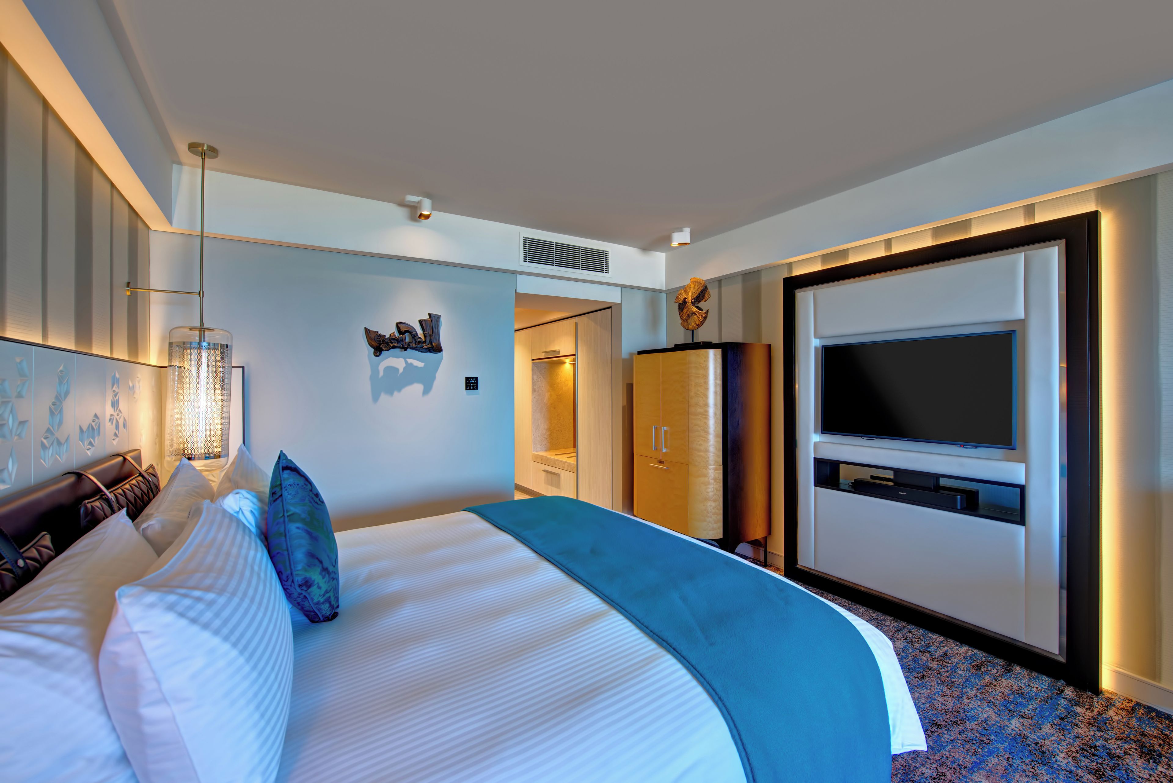 A modern hotel room with a large bed, a flat-screen TV, a wardrobe, and a decorative wall piece.