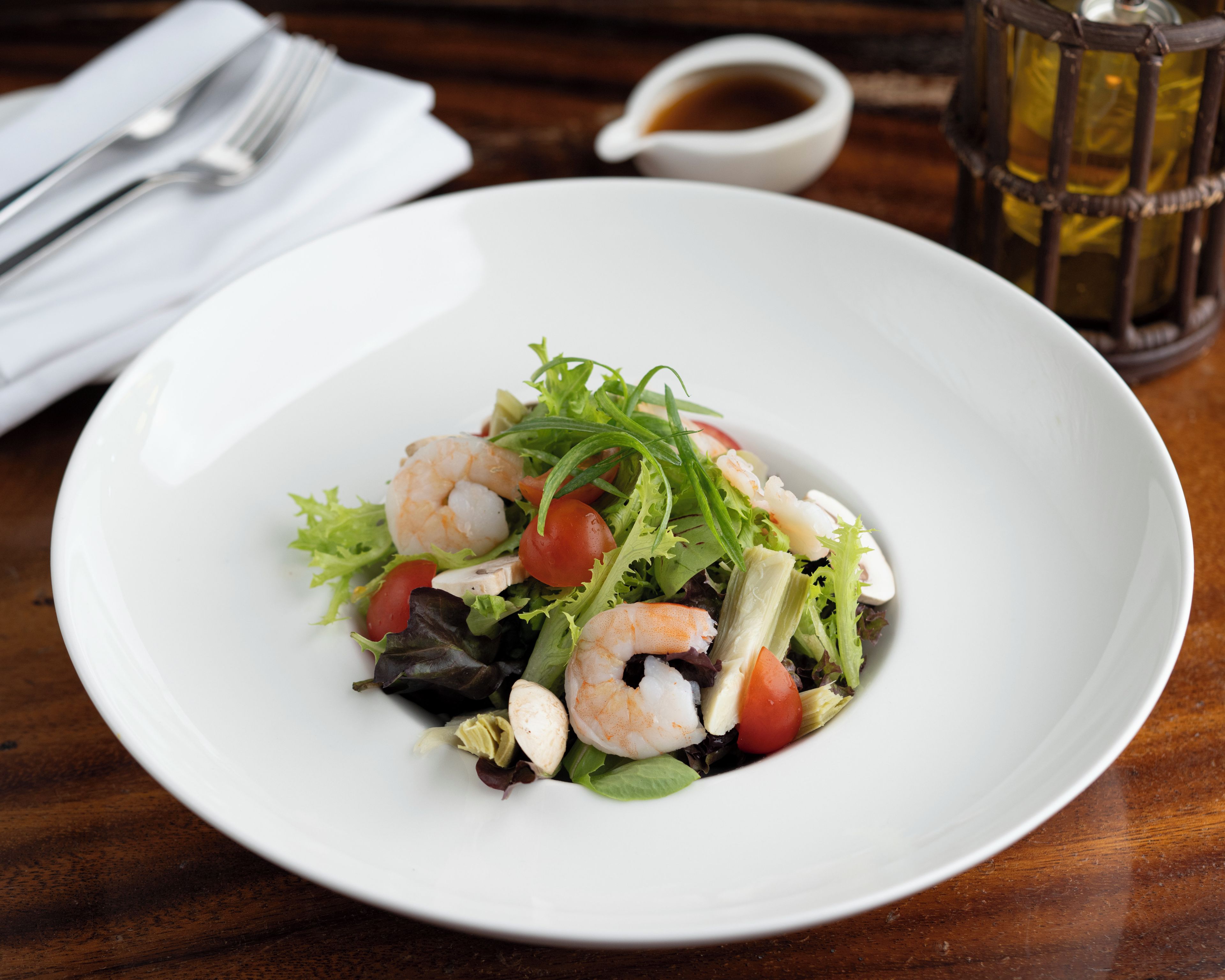 A white plate with a salad on a wooden table.