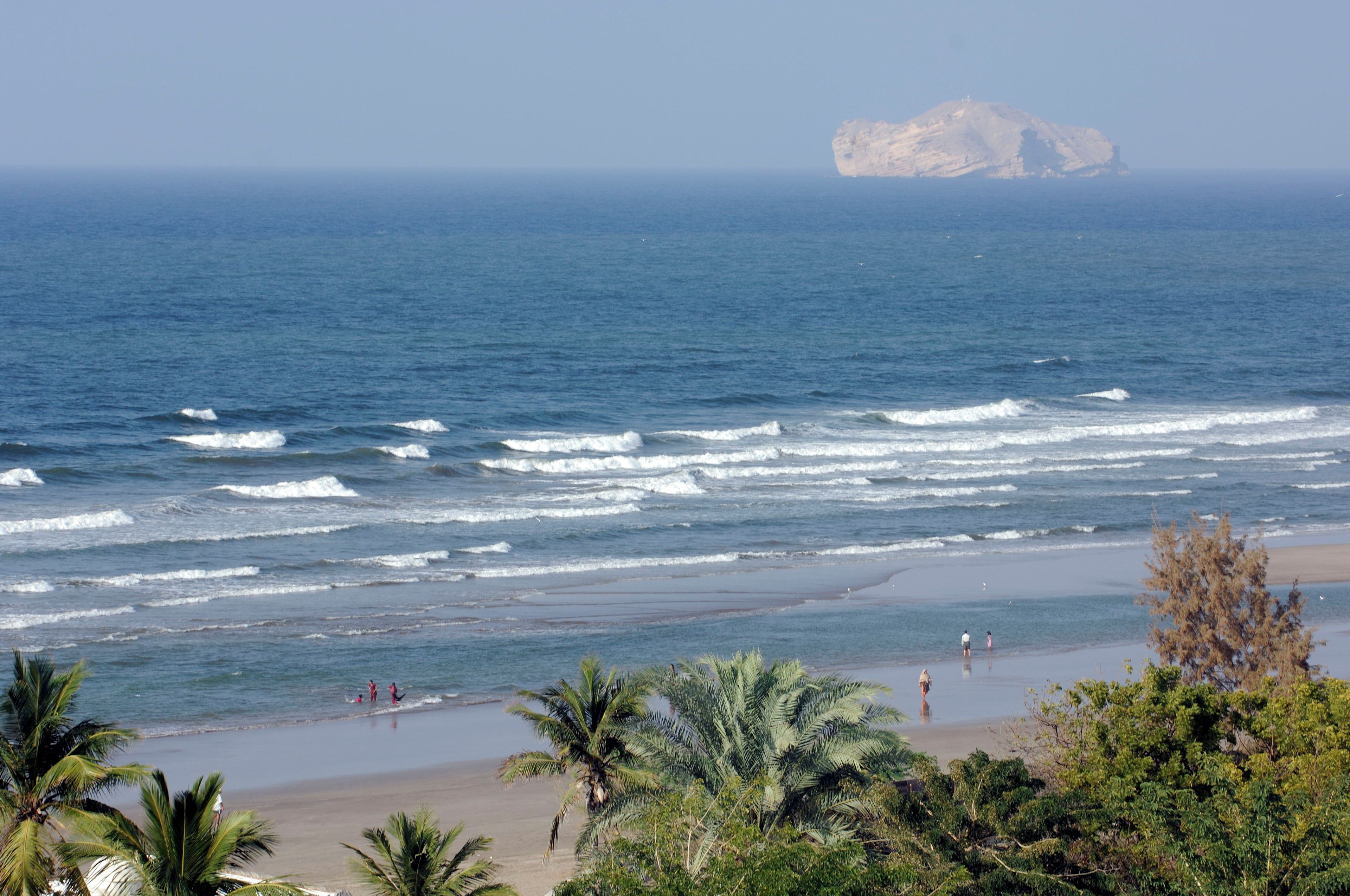 Une plage avec des vagues, des palmiers et une île rocheuse qui se dessine à l’horizon.