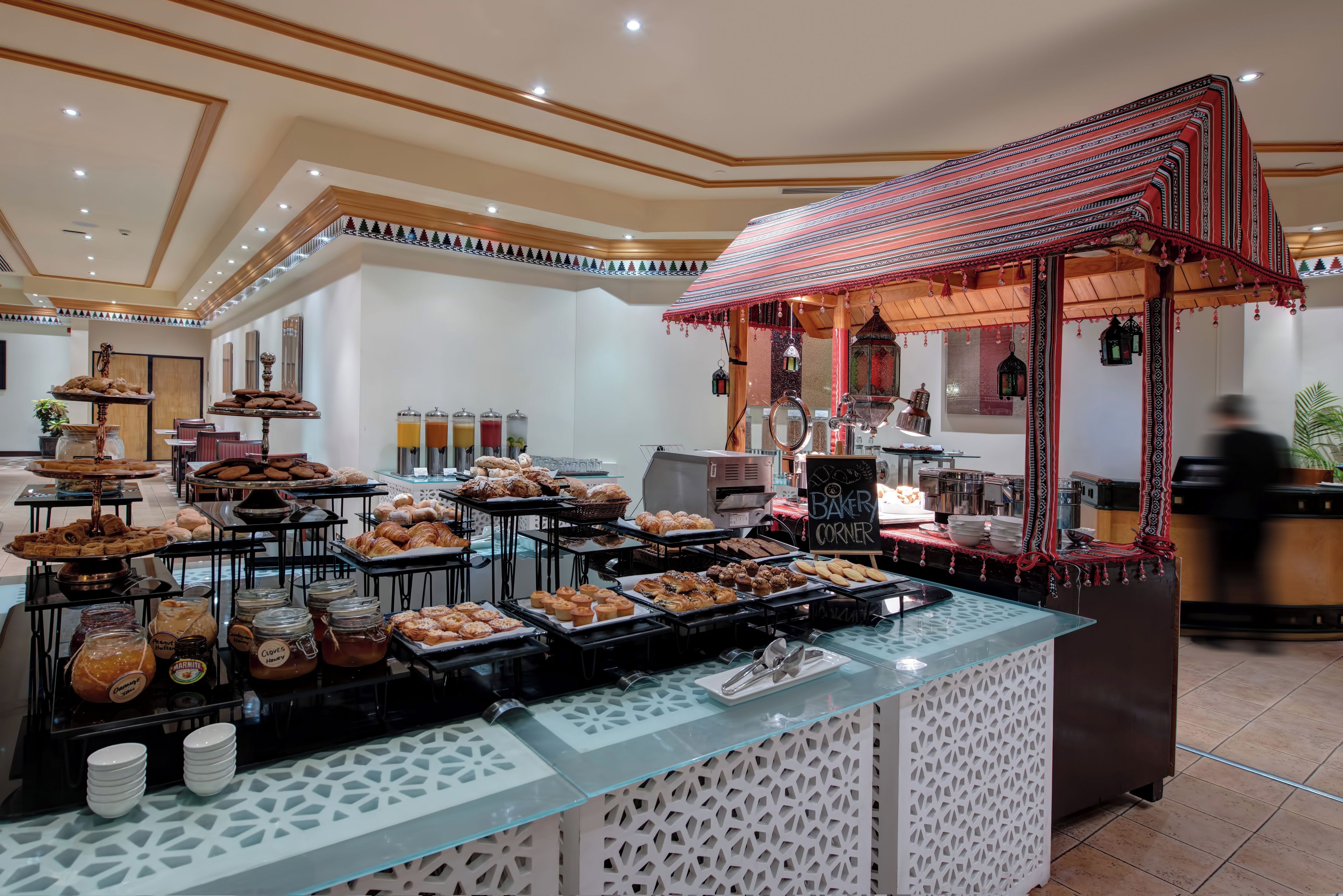 Uma área de buffet com diversas opções de pães e doces, um espaço para café e um canto de pastelaria.