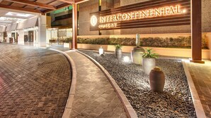A hotel entrance with a sign reading "INTERCONTINENTAL MUSCAT" and a paved walkway leading to the lobby.