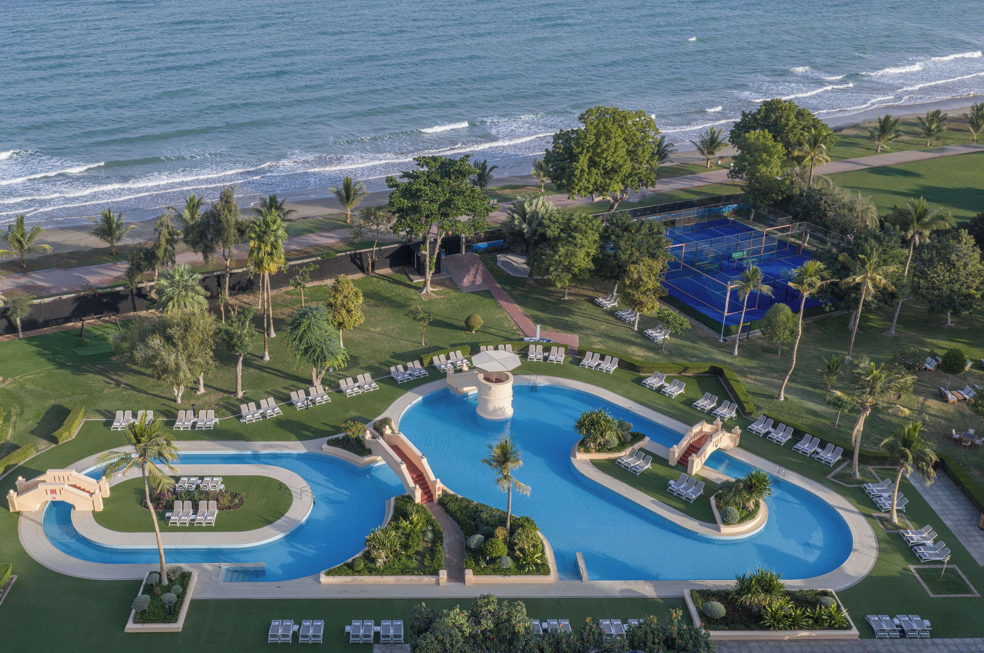 Een resort met een groot zwembad, ligbedden, palmbomen en uitzicht op de oceaan.