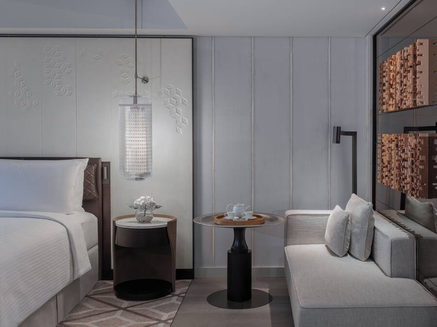 Een moderne hotelkamer met een bed, een ronde tafel met dienblad, een bank en een decoratief wandpaneel.