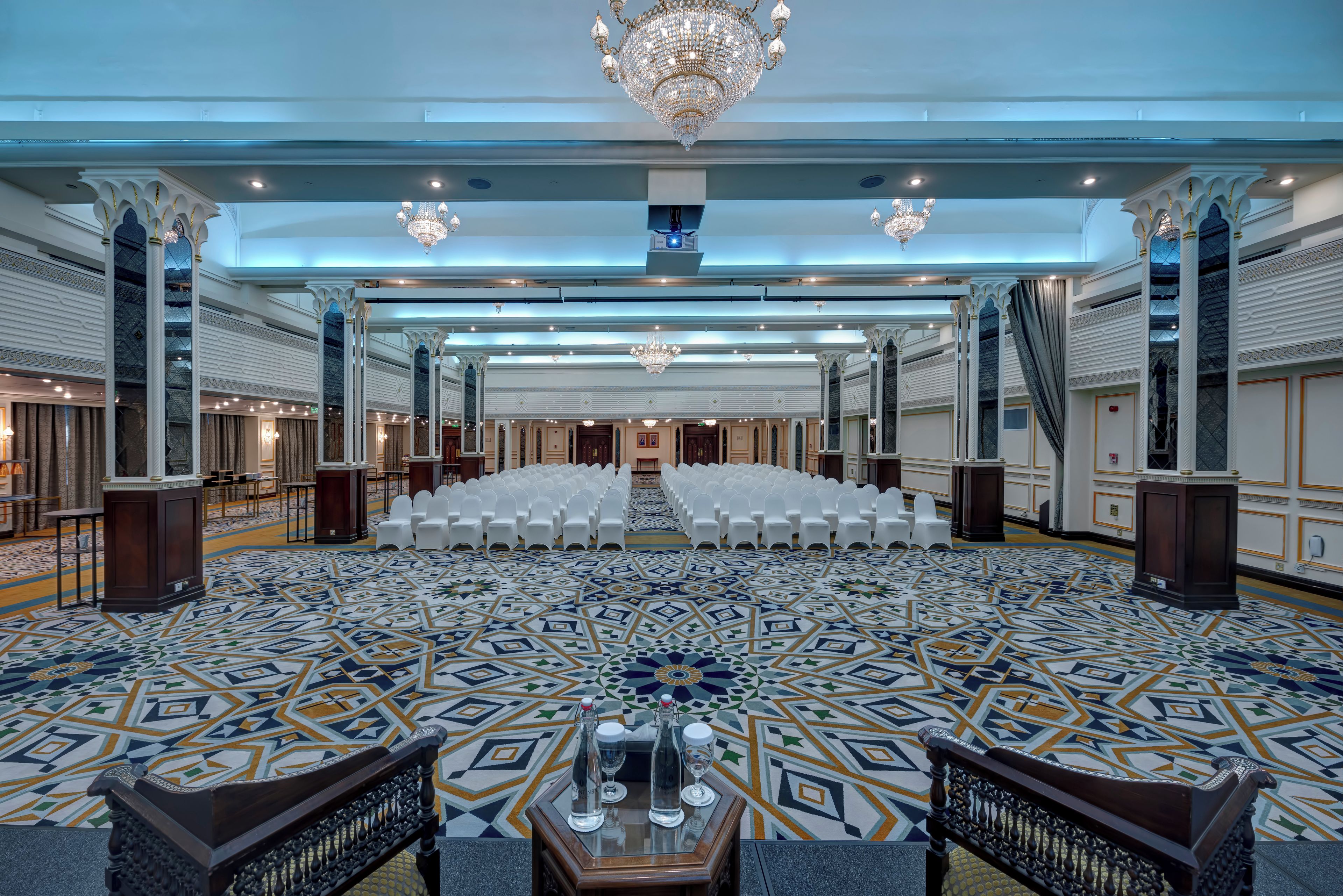 A spacious hall with rows of white chairs, a patterned floor, and a chandelier.