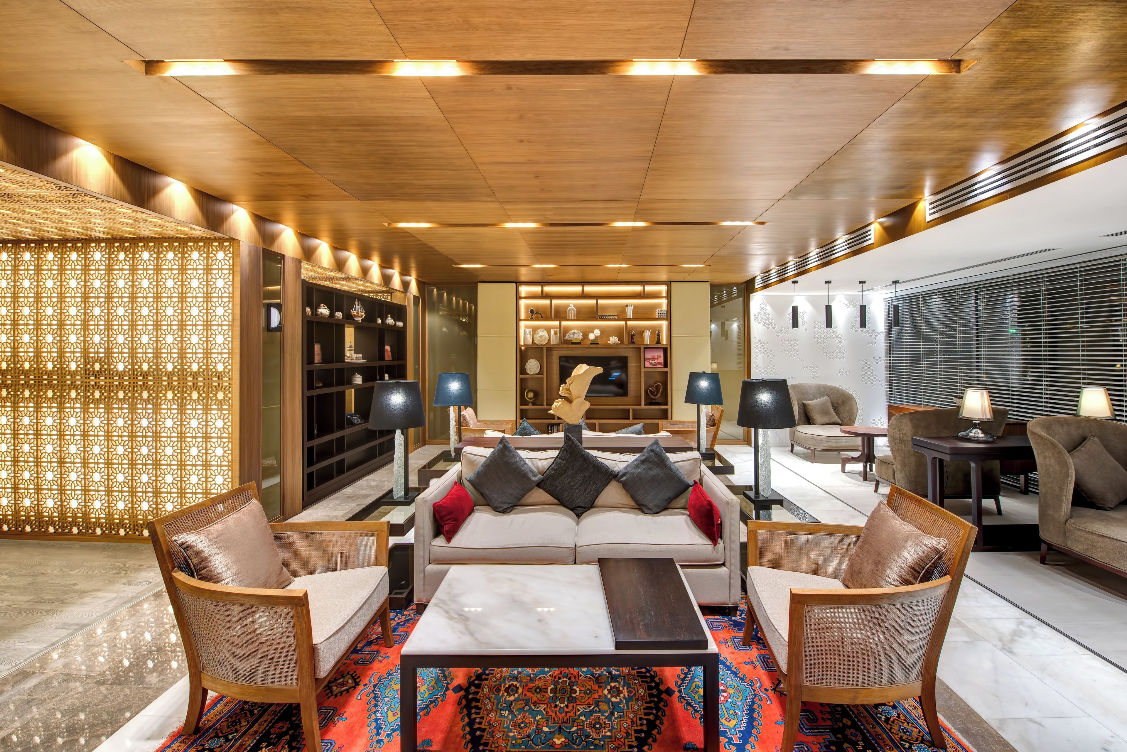 A modern living room with a sofa set, a coffee table, and a TV. There are decorative shelves and a patterned rug.