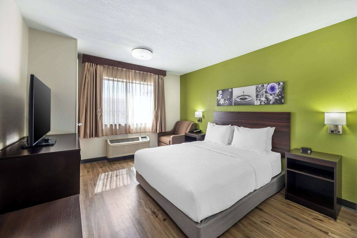 Une chambre d’hôtel dotée d’un grand lit, d’un téléviseur à écran plat, d’un bureau, d’une chaise, d’une table de chevet et d’une lampe fixée au mur.
