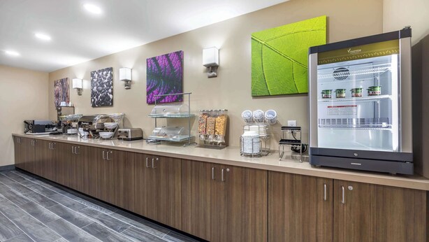 A modern kitchen area with a refrigerator, coffee machine, and various food items.