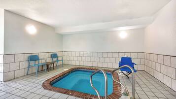 A swimming pool with a tiled floor, a brick border, and a metal ladder. There are blue chairs and a blue chair in the background.