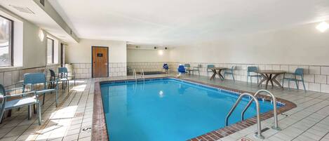 A swimming pool with a tiled floor, surrounded by blue chairs and tables.