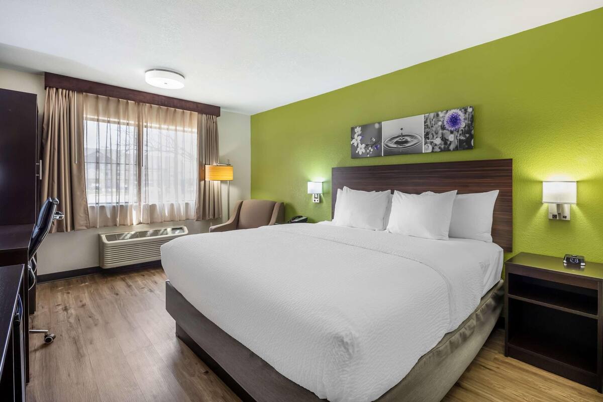 A hotel room with a large bed, a desk, a chair, a lamp, and a wall-mounted artwork.