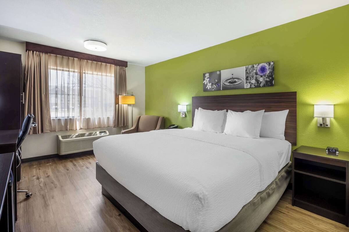 Une chambre d’hôtel avec un grand lit, un bureau, une chaise et une fenêtre avec des rideaux.