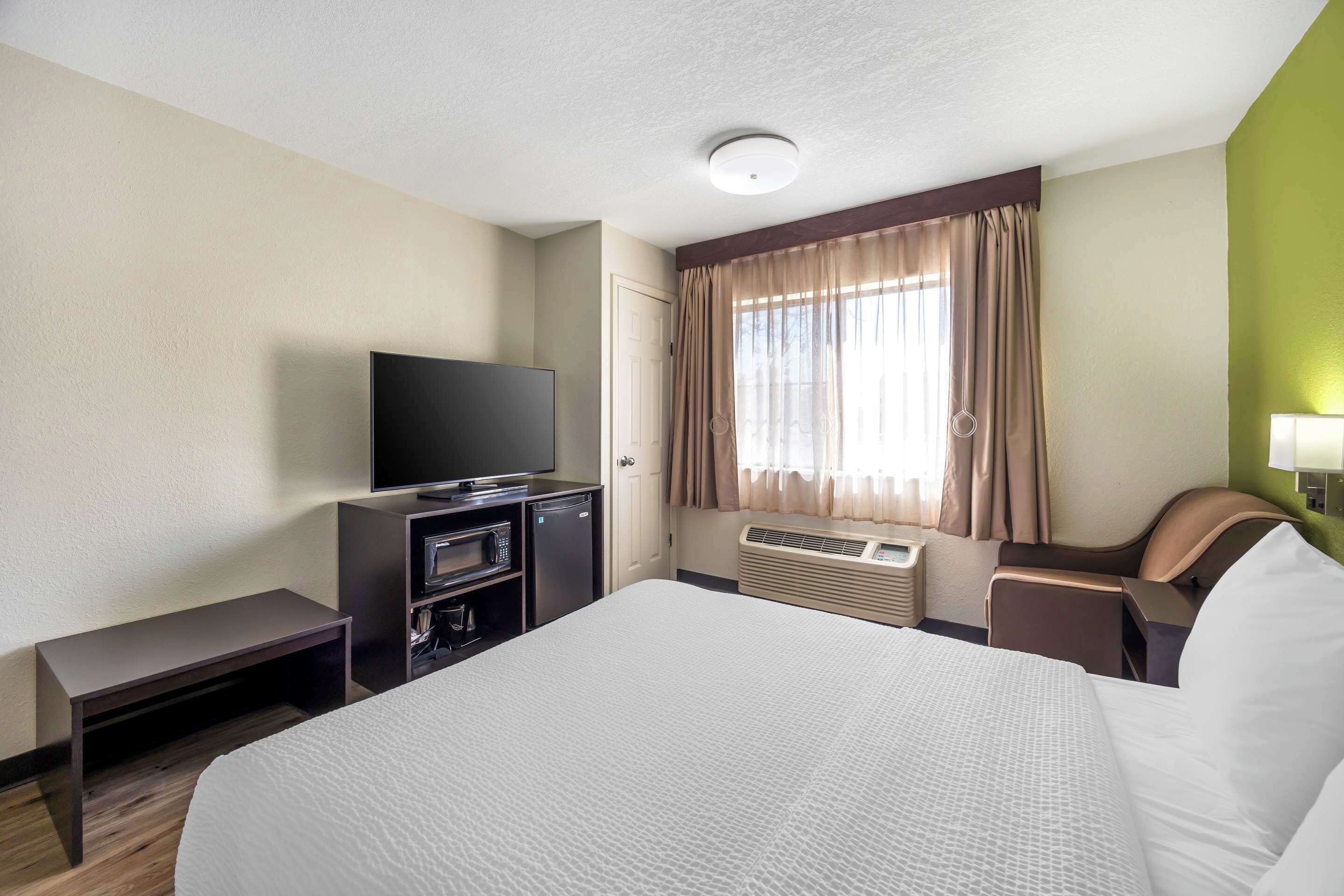 A hotel room with a large bed, a flat-screen TV, a desk with a chair, and a window with curtains.
