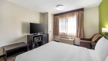 A hotel room with a large bed, a flat-screen TV, a desk with a chair, and a window with curtains.