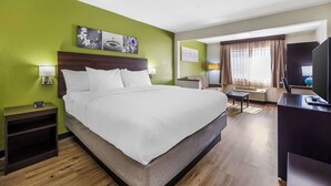 A hotel room with a large bed, a desk, a chair, a television, and artwork on the walls.