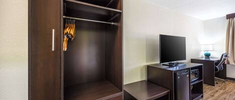 Habitación de hotel con un armario de madera, un escritorio con televisor de pantalla plana, un mini refrigerador y una lámpara.