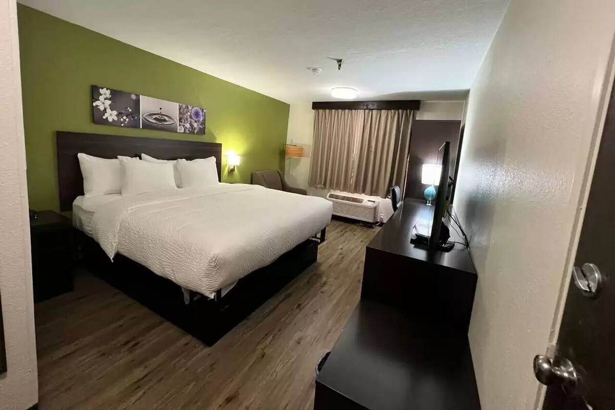 A hotel room with a bed, a desk, a chair, a lamp, and a window with curtains.