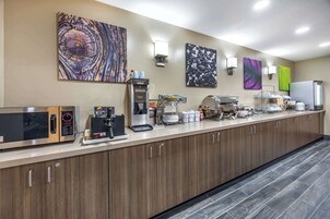 Una cocina moderna con microondas, cafetera y plancha para gofres. Hay luces empotradas en la pared y obras de arte sobre la encimera.