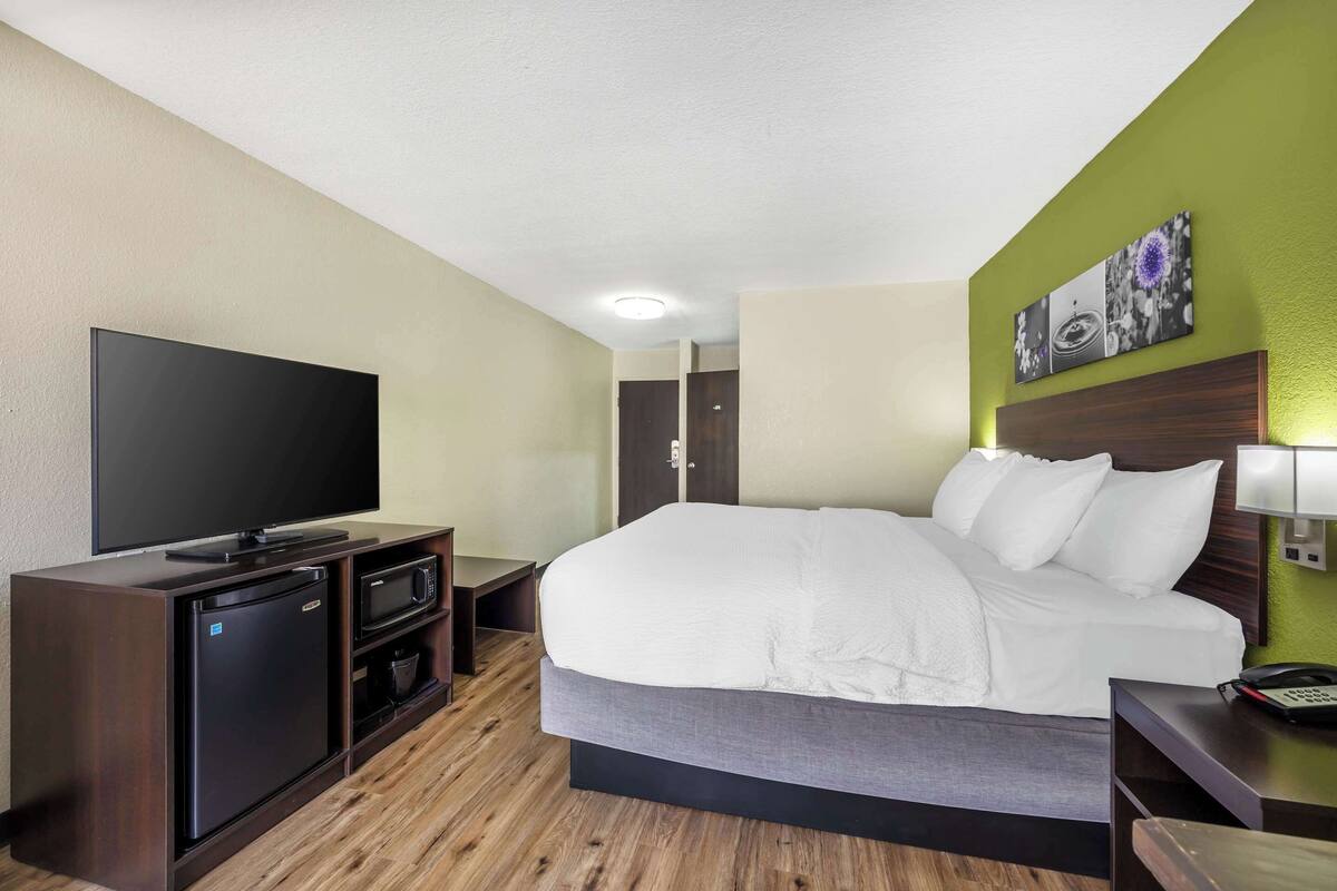 Une chambre d’hôtel avec un lit, une télévision, un mini-réfrigérateur et un plancher en bois.