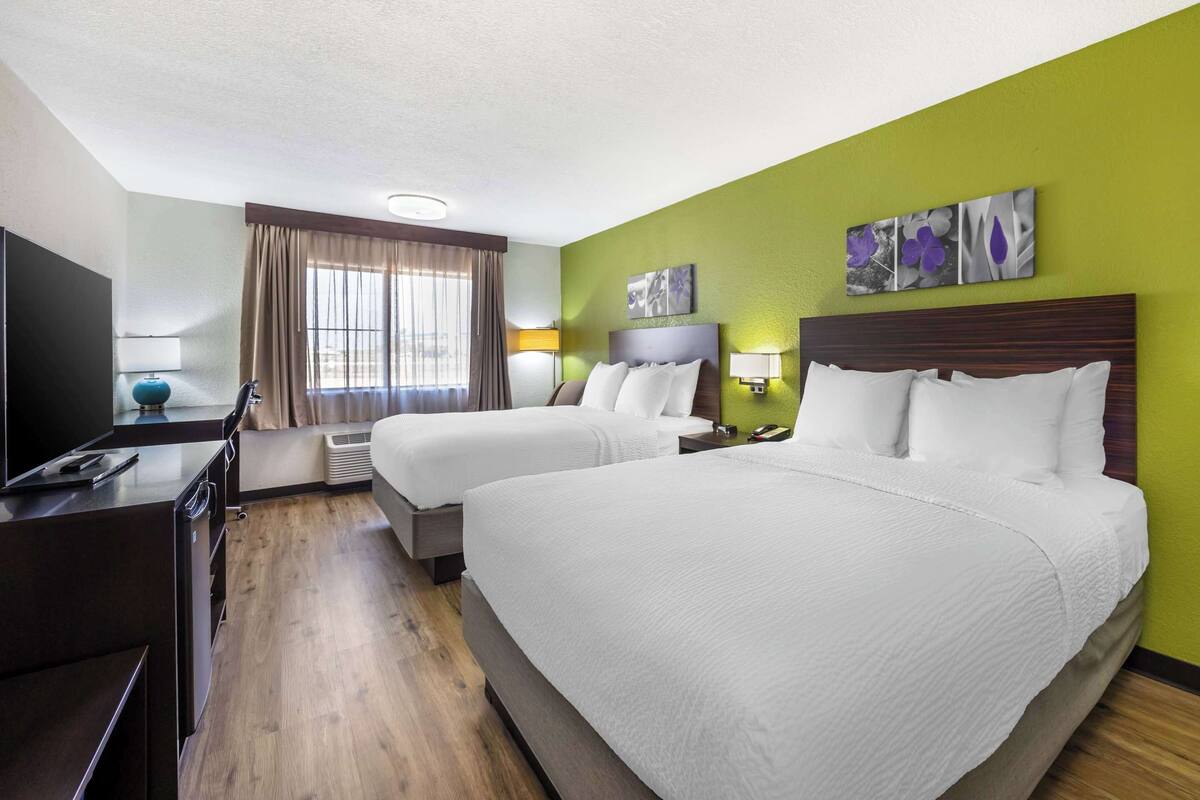 Une chambre d’hôtel avec deux lits, une télévision, un bureau et une fenêtre avec des rideaux.