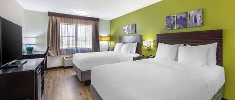 Habitación de hotel con dos camas, televisión, escritorio y ventana con cortinas.