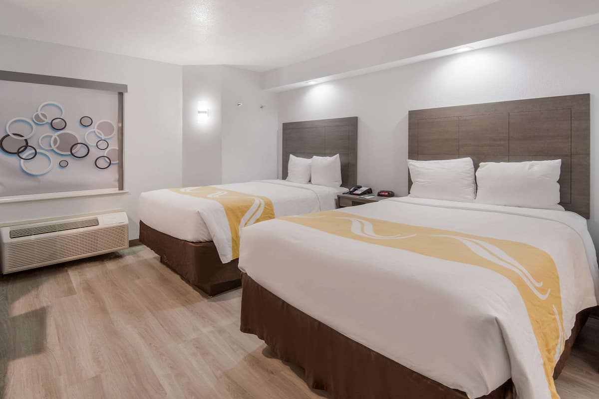 A hotel room with two beds, a wall-mounted air conditioner, and a decorative wall piece.