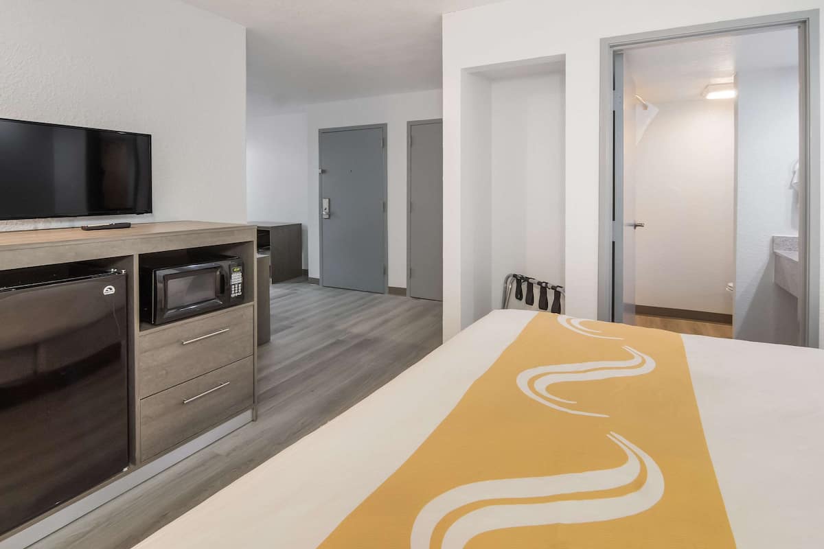 A hotel room with a bed, a TV, a microwave, and a refrigerator. There are doors leading to other rooms and a bathroom.