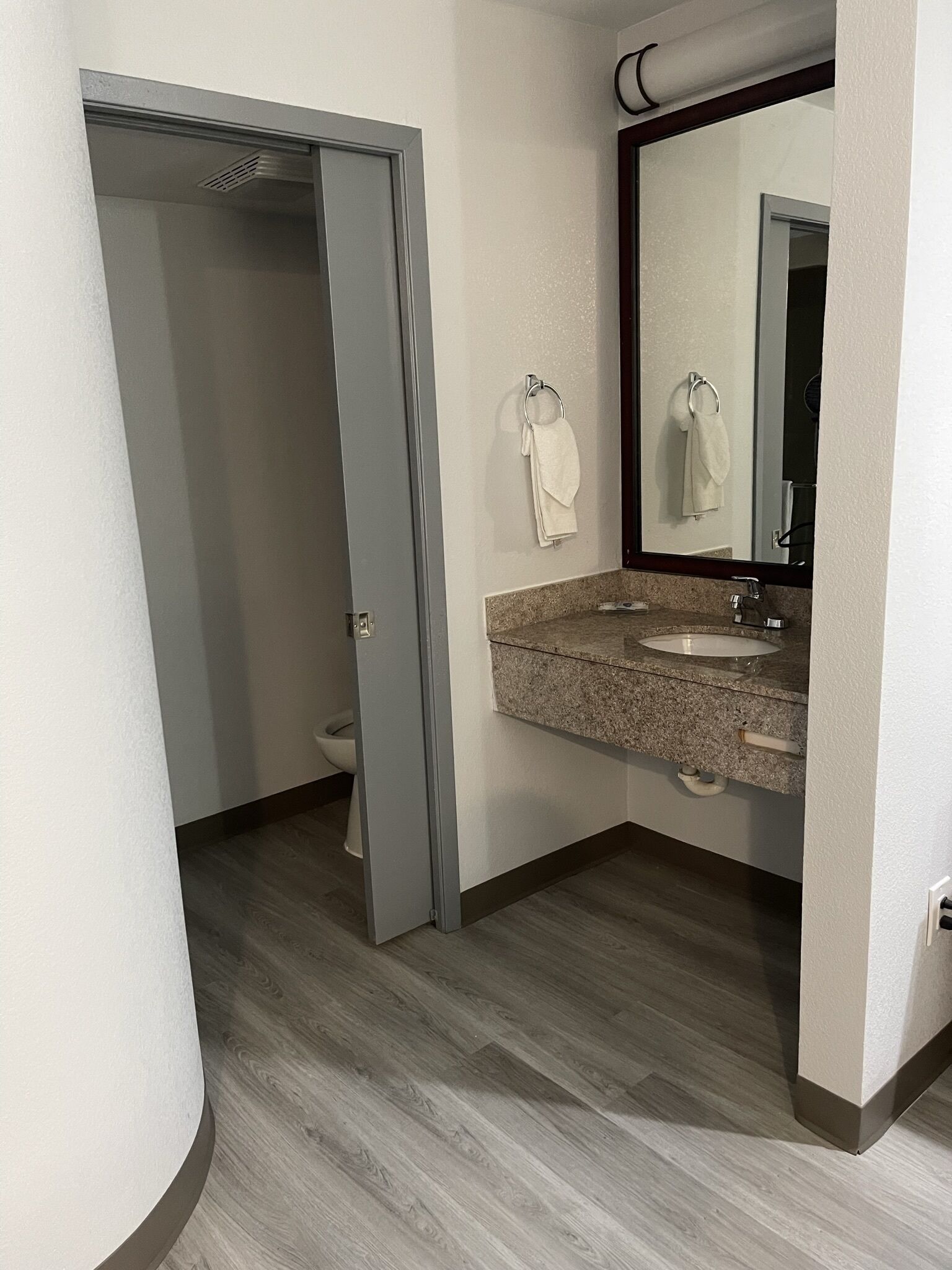 A bathroom with a granite countertop, a sink, a mirror, and a toilet visible through an open door.