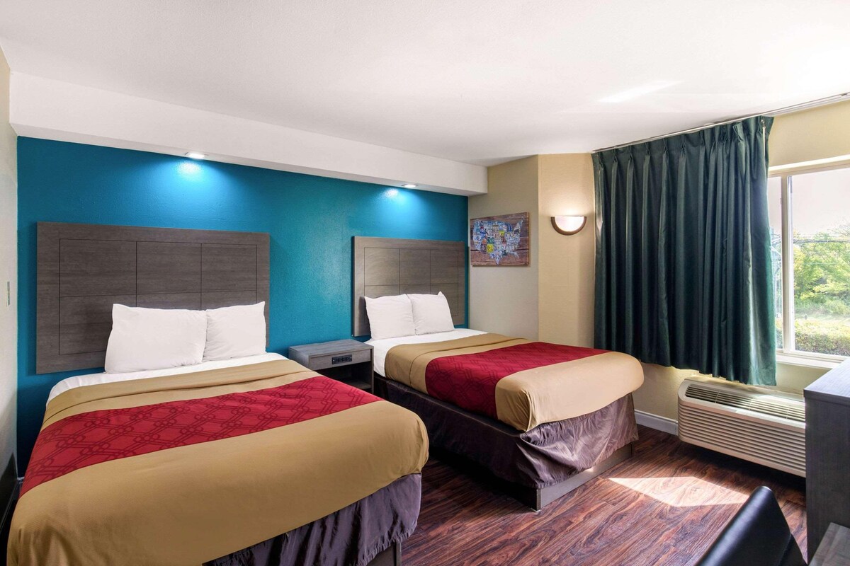 A hotel room with two beds, a nightstand, a desk, and a window with curtains.