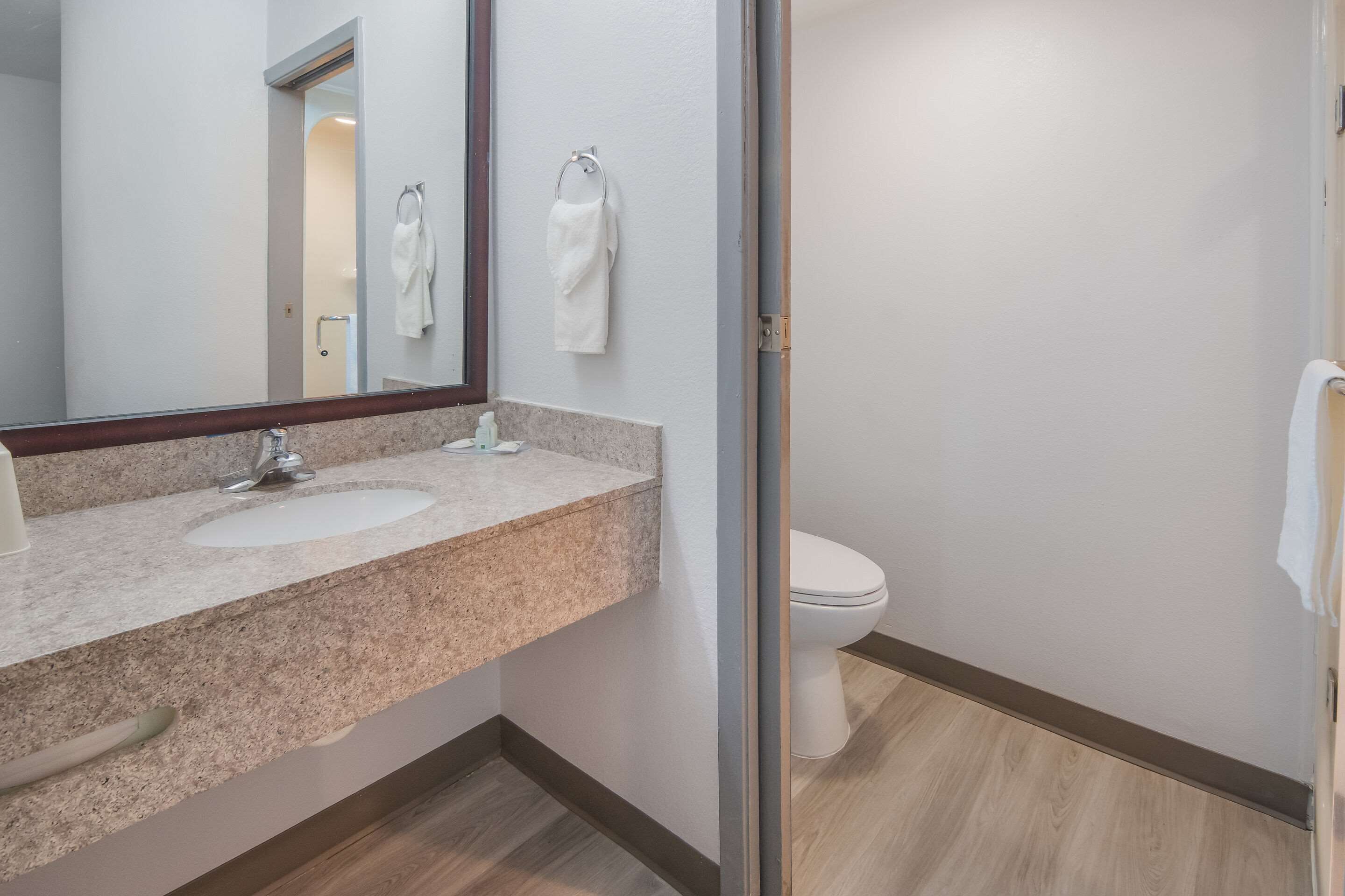 A bathroom with a granite countertop, a sink, a mirror, a toilet, and a towel hanging on the wall.