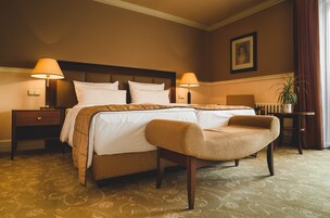 Camera d'albergo con un letto grande, due comodini con lampade, una sedia, un tavolino e una pianta in vaso.