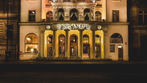 A historic building with a prominent entrance, a balcony with flags, and the name "ESPLANADE" displayed above the doors.