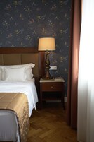 Una habitación de hotel con cama, mesita de noche con lámpara y un papel tapiz estampado con motivos florales.