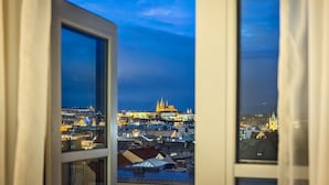 Vista desde una ventana sobre un paisaje urbano al anochecer, con edificios iluminados y una catedral destacada.