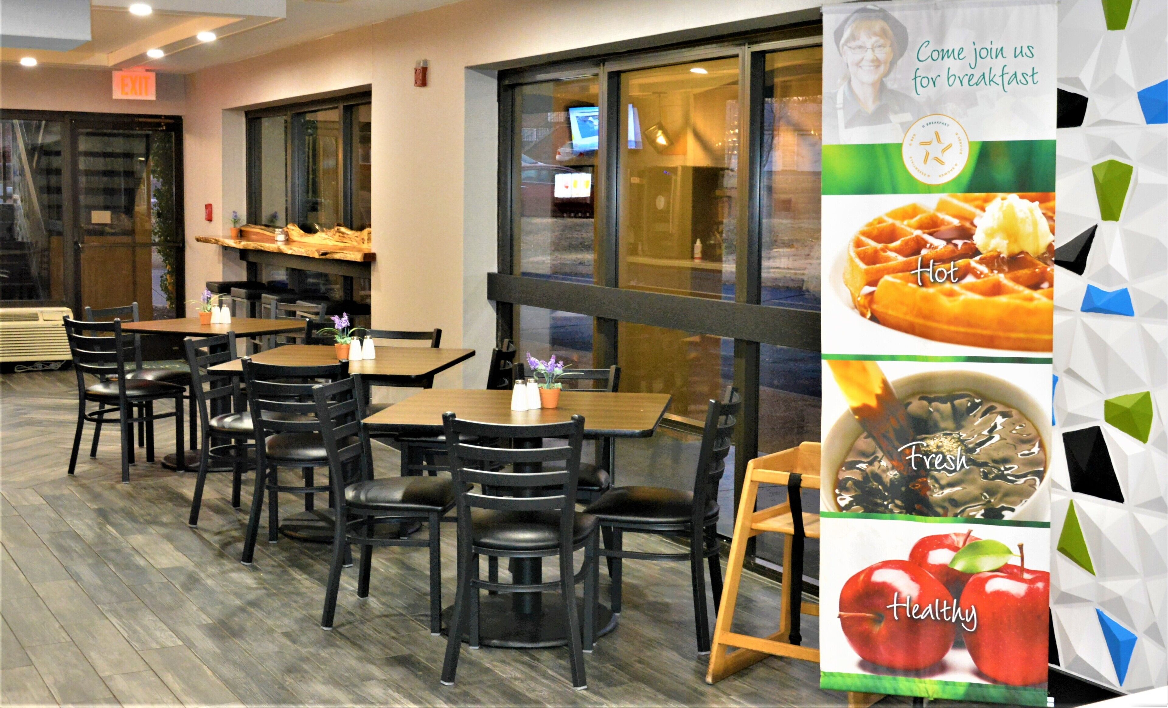 A restaurant interior with wooden tables and chairs, a large window, and a poster advertising breakfast.