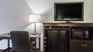 Habitación de hotel con escritorio, silla, lámpara, televisor, refrigerador y microondas.