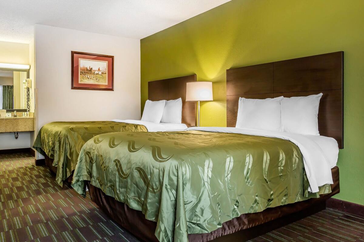 Habitación de hotel con dos camas, un espejo grande, un cuadro en la pared y una pared verde.