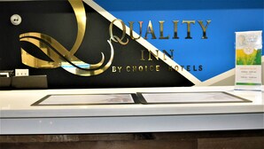Una mesa de recepción con un letrero que dice "QUALITY INN BY CHOICE HOTELS" y un expositor de folletos.