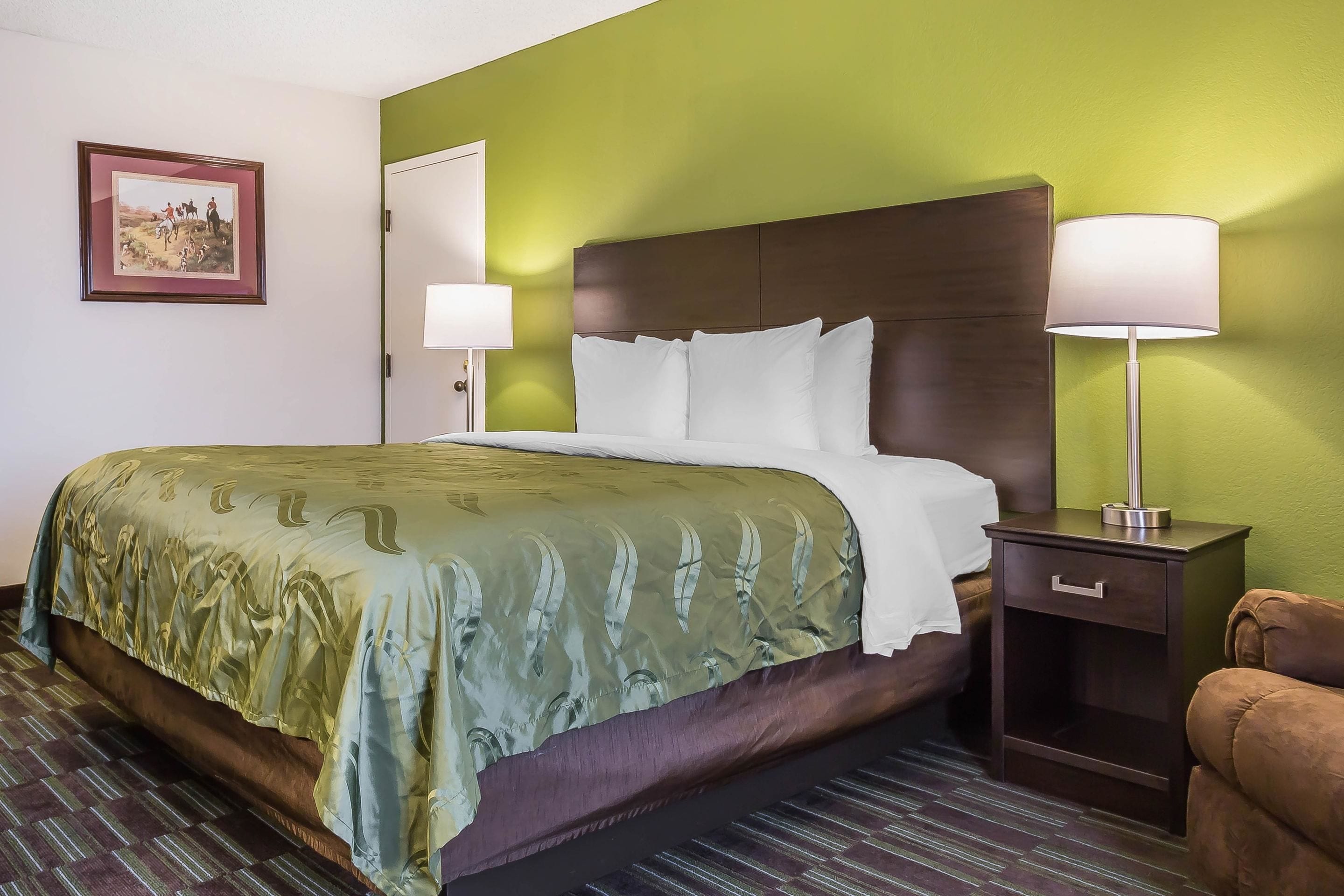 A hotel room with a bed, nightstands, a lamp, and a framed picture on the wall.