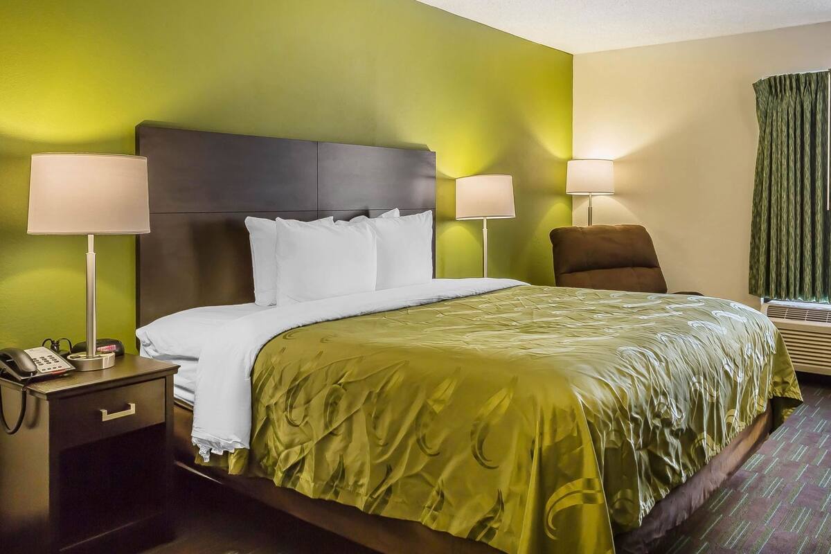 Habitación de hotel con cama, dos lámparas de noche, una mesita de noche con teléfono, una silla y una ventana con cortinas.