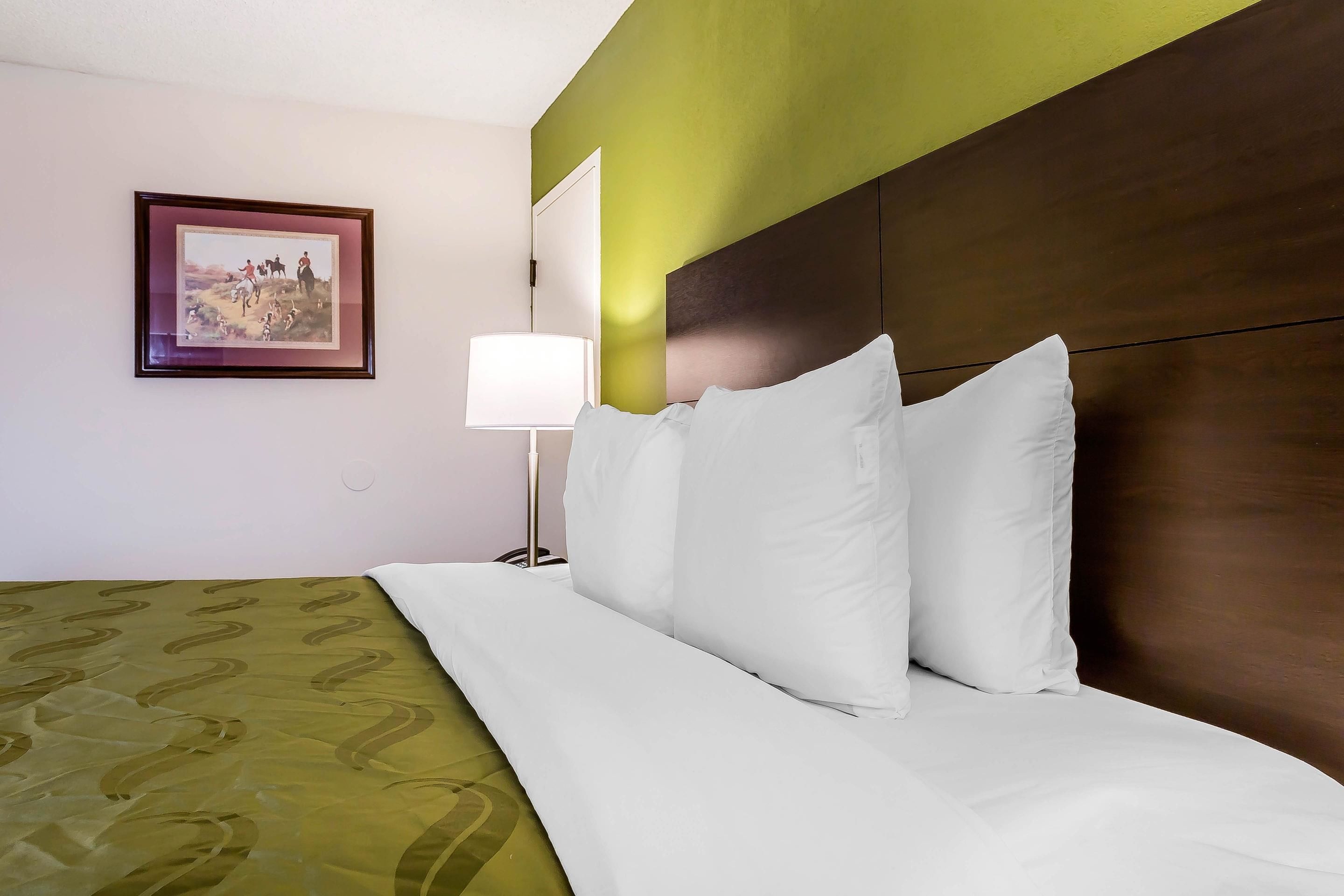 A neatly made bed with white linens, a green patterned bedspread, and a framed picture on the wall.